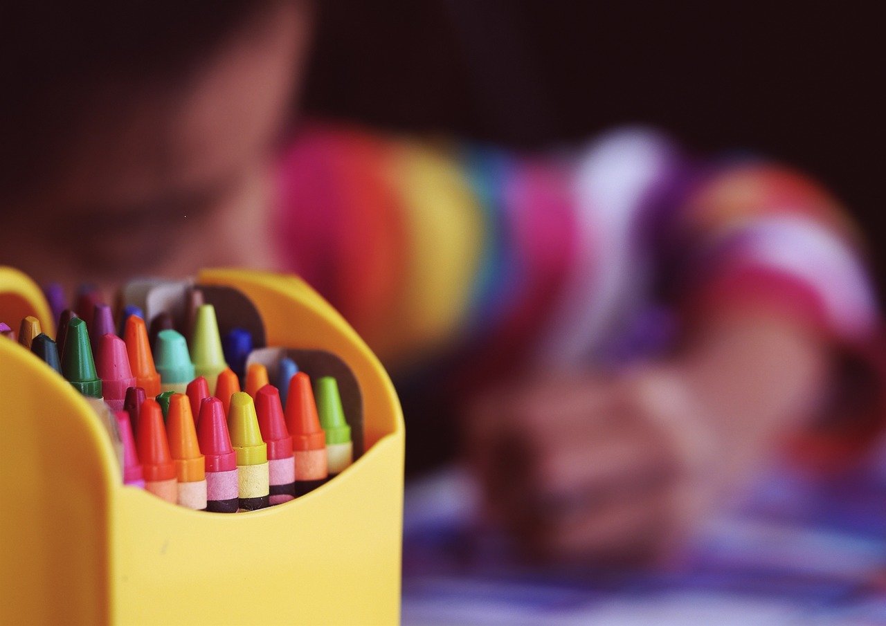 Colourful crayons in a pot with a child drawing behind