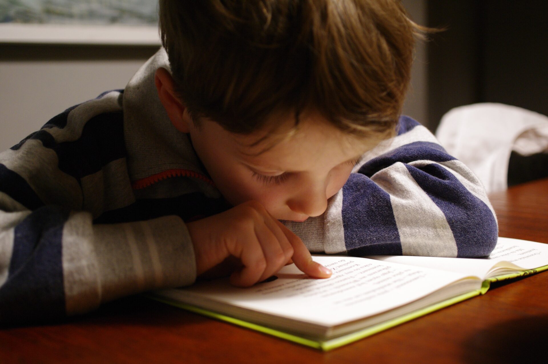 Small boy leaning over a book and reading