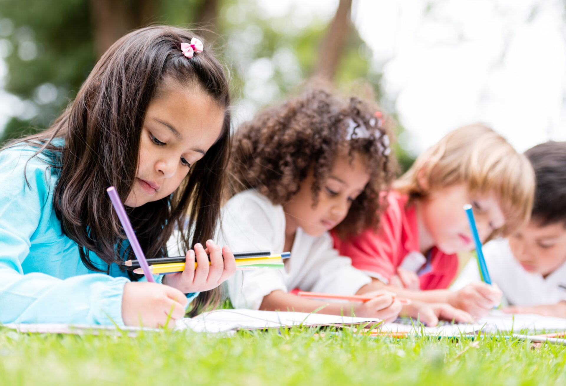 A row children lying on some grass writing