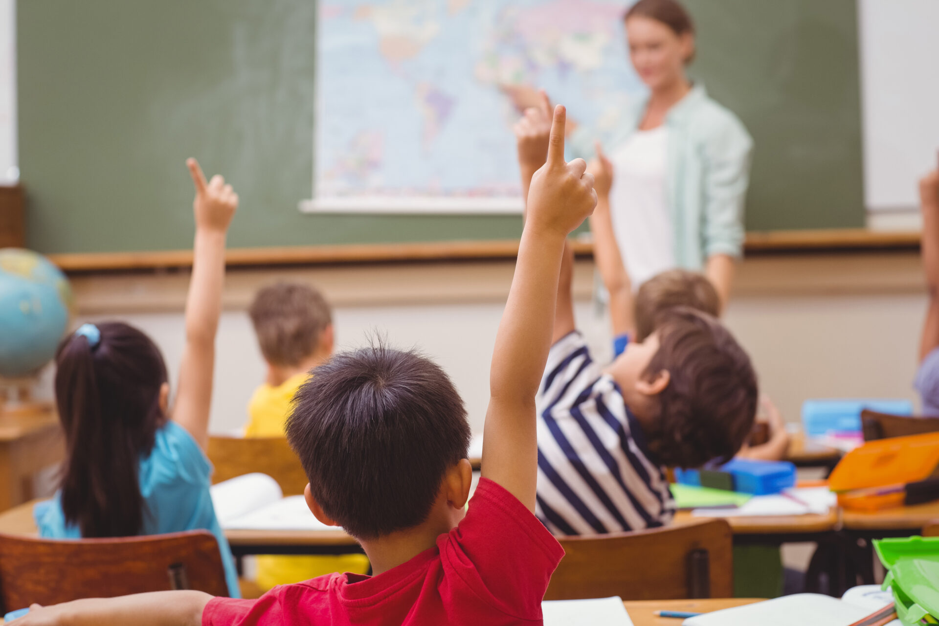 Teacher at a blackboard with children at their desks with hands up