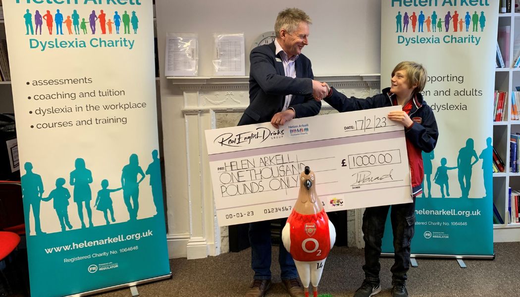 Young Charlie presents our CEO Andy Cook with a giant cheque for £1000 standing behind a model hen painted to look like Arsenal footballer Thierry Henry